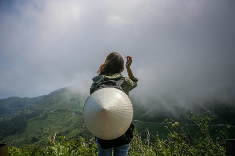 Back view of a woman traveler in misty mountains wearing an Asian conical hat.